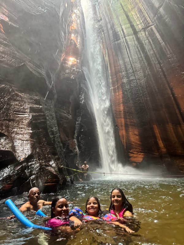 Família com boias na água, diante da queda alta do Santuário descendo pelo paredão de arenito