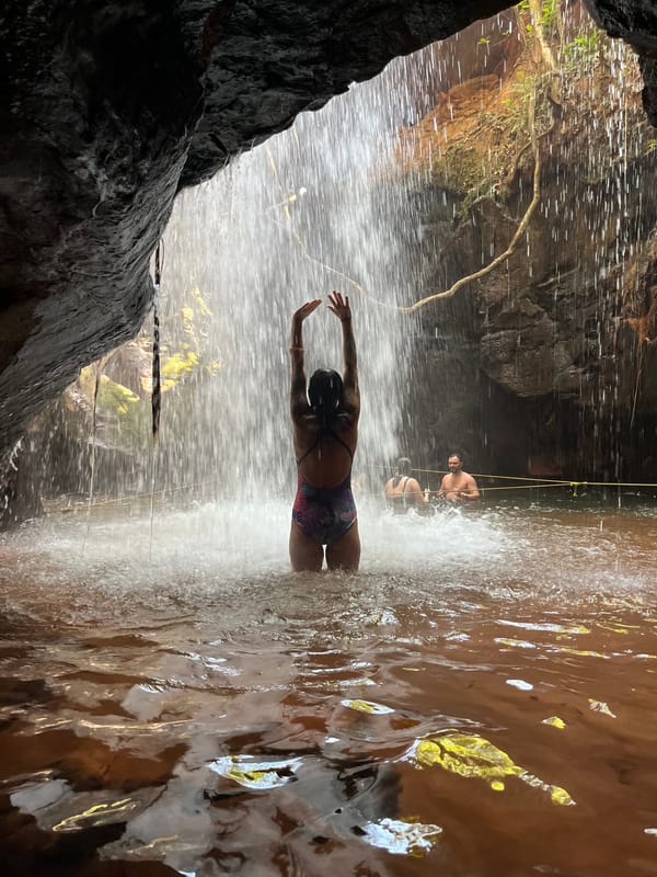 Mulher de braços erguidos sob a queda dentro da Cachoeira da Caverna