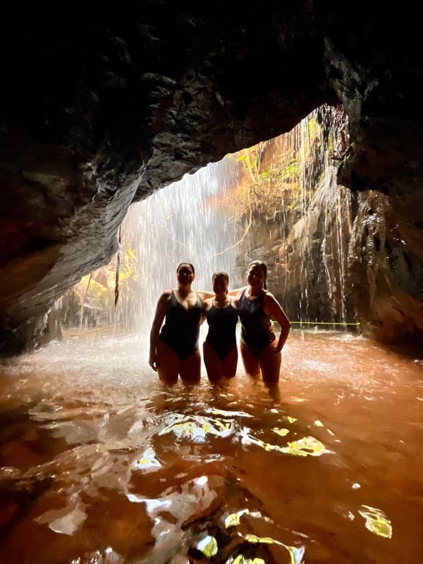 Três pessoas na água dentro da gruta da Caverna, contra a luz da queda que cai na entrada