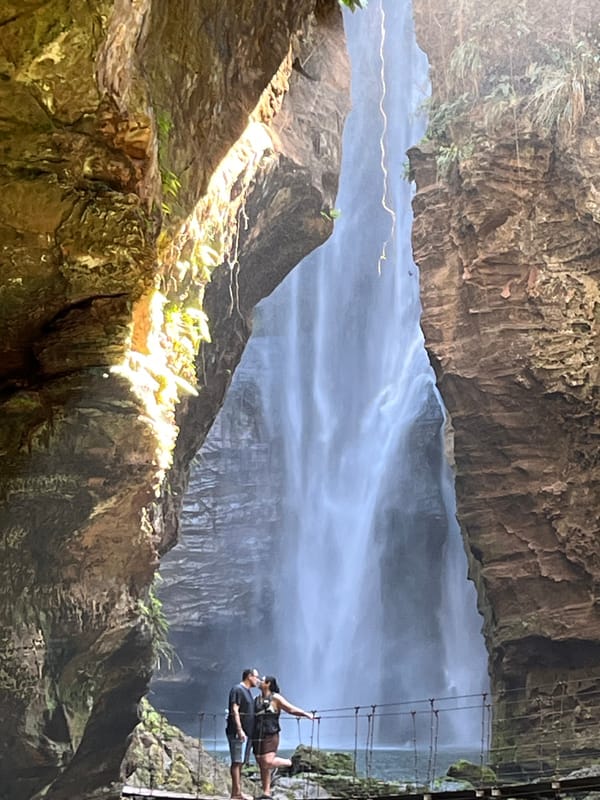 Queda alta descendo por um paredão de arenito, com um casal na passarela ao pé dela