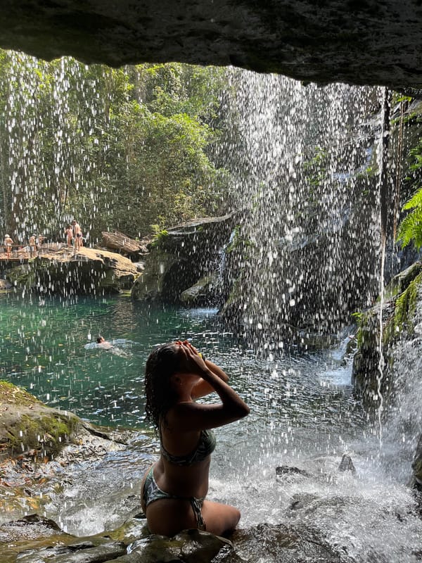 Mulher na água sob uma cortina de quedas finas que descem da borda da gruta