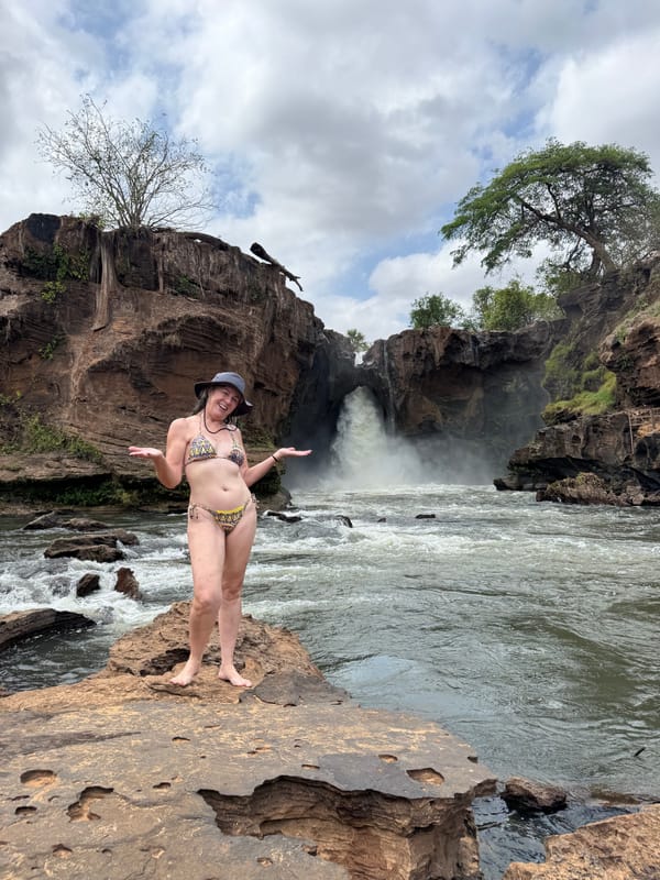 Mulher de pé numa pedra diante de uma queda, sob céu com nuvens
