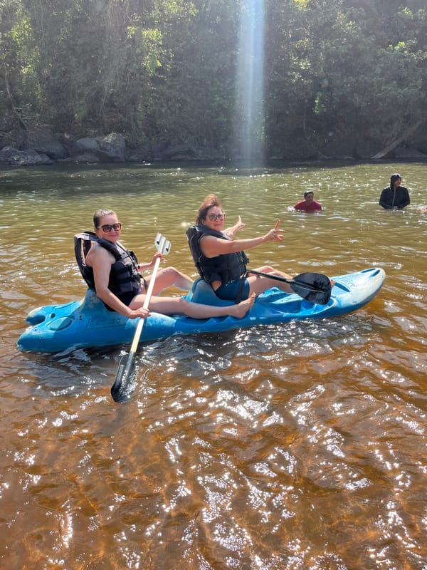 Duas pessoas num caiaque azul na água do rio, com uma queda fina ao fundo
