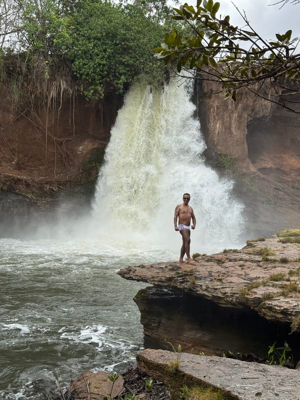 Homem de pé na beira da laje, diante da queda volumosa da Cachoeira do Prata
