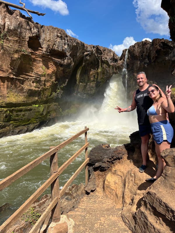 Casal posando no corrimão de madeira ao lado da queda volumosa da Cachoeira do Prata