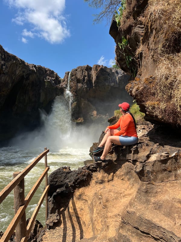 Homem de boné vermelho sentado nas pedras diante da Cachoeira do Prata