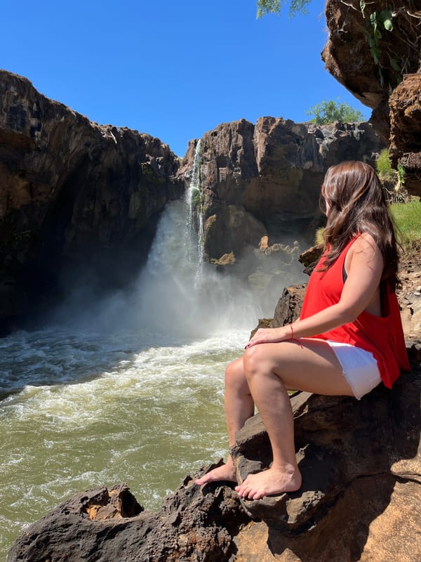 Mulher sentada nas pedras olhando a queda da Cachoeira do Prata, sob céu azul