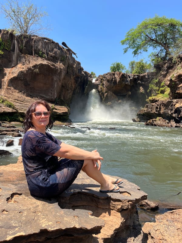 Mulher sentada numa laje à beira do rio, com a Cachoeira do Prata ao fundo