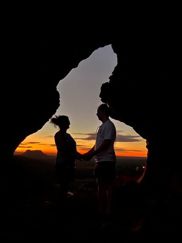Silhueta de um casal de mãos dadas no buraco do Portal, contra o pôr do sol