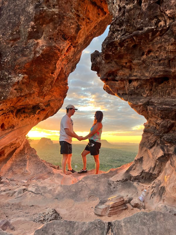 Casal de mãos dadas dentro do arco do Portal da Chapada ao pôr do sol