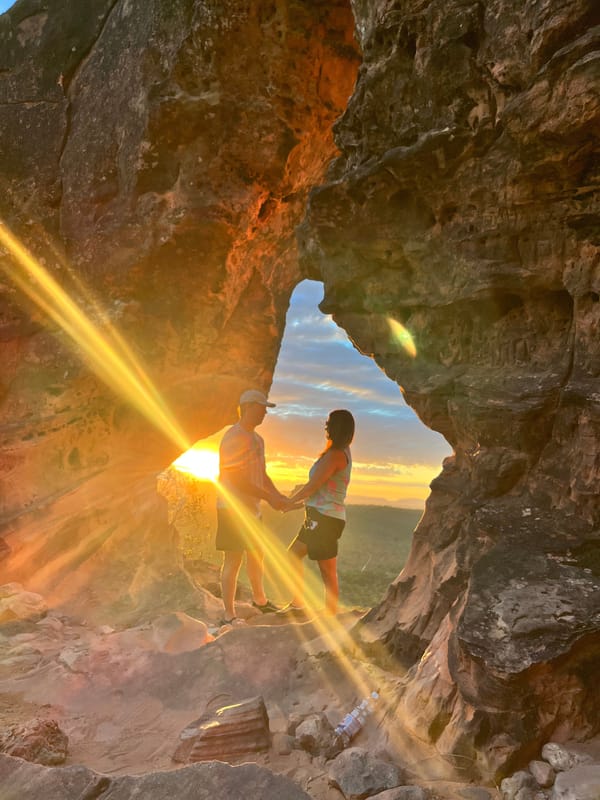 Raio de sol atravessando o arco de arenito do Portal da Chapada, com um casal dentro do vão