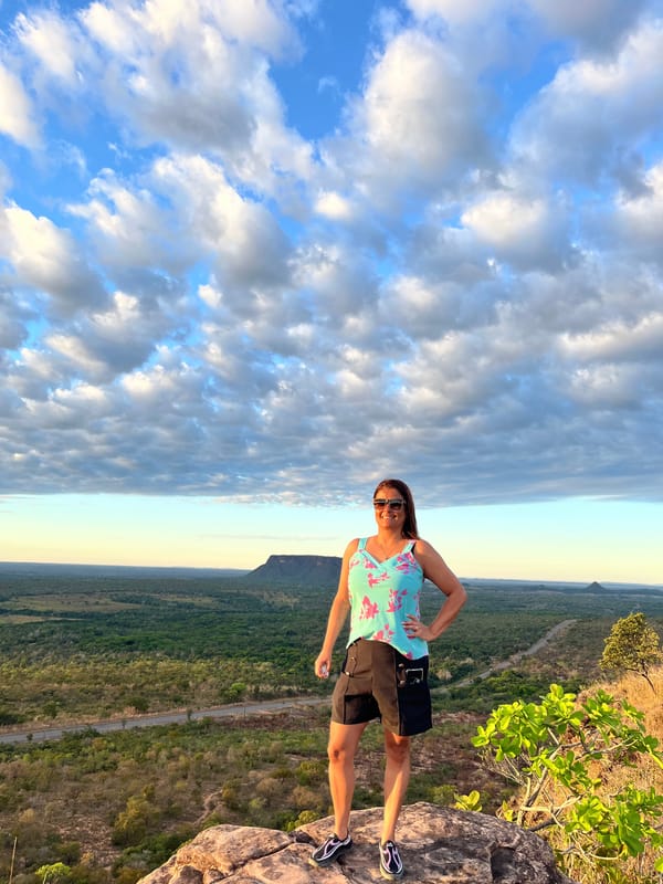Mulher de pé numa pedra no alto do Portal, com o cerrado e as mesas ao longe e o céu cheio de nuvens