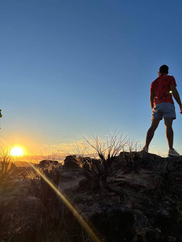 Homem de pé numa pedra contra o sol baixo, no Portal da Chapada