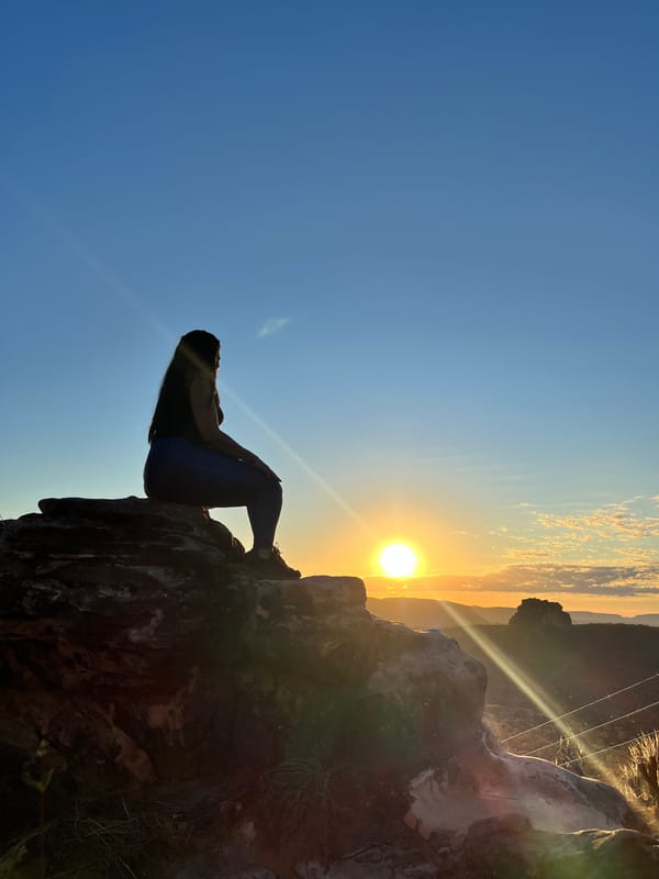 Silhueta de uma mulher sentada numa pedra olhando o sol baixo, no Portal da Chapada