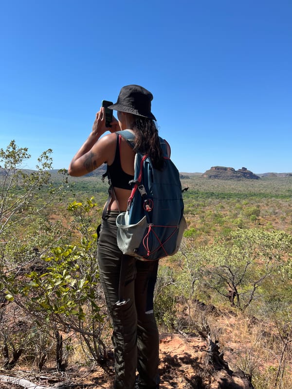 Mulher de chapéu fotografando o cerrado e as mesas do alto de uma pedra