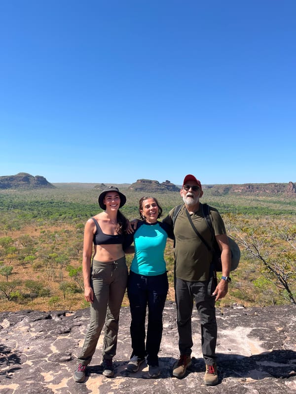 Três caminhantes sorrindo numa laje de pedra, com as mesas no horizonte