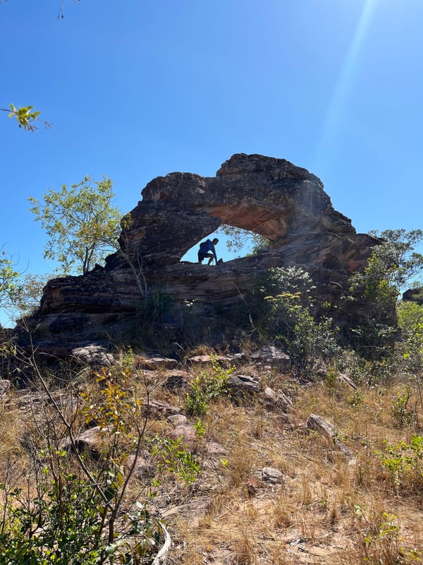 Arco de pedra no alto de um rochedo sobre o cerrado, com uma pessoa dentro do vão