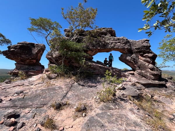Arco de arenito sobre um lajedo, com duas pessoas sob o vão e o cerrado em volta