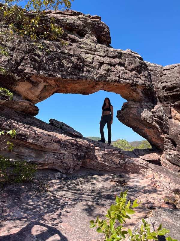 Mulher de pé sob o vão de um arco de arenito, emoldurada pela pedra