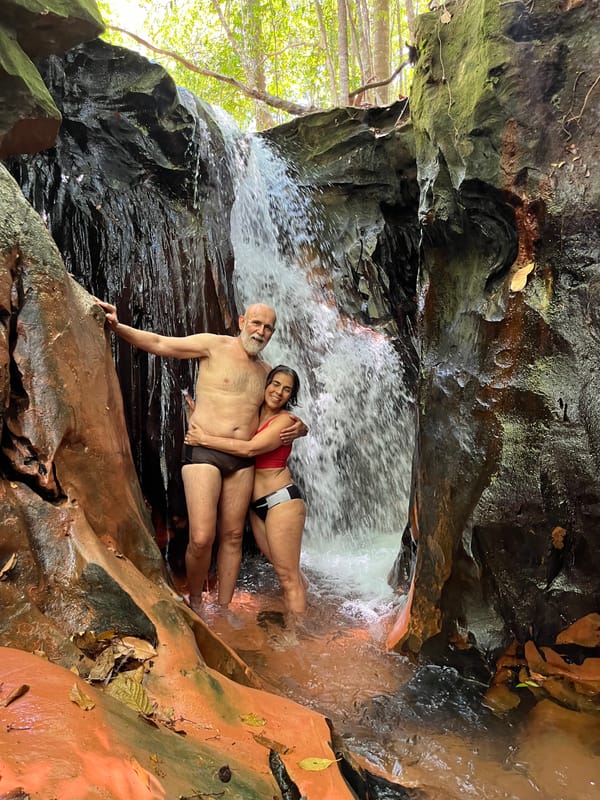 Casal abraçado ao lado de uma queda d’água estreita entre paredões de arenito