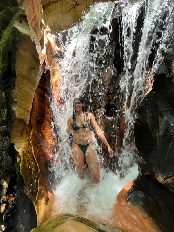 Mulher sob uma queda d’água que desce entre paredões de arenito numa fenda