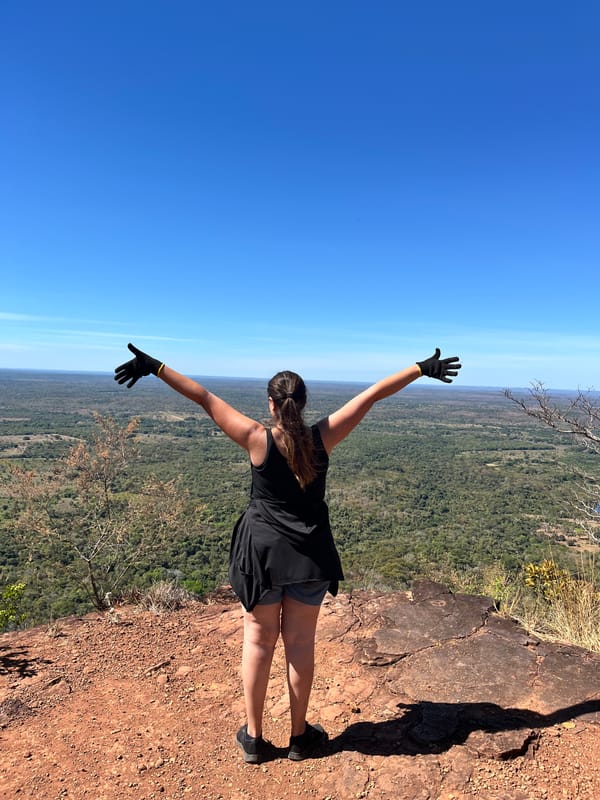 Mulher de costas e de braços abertos na beira do Morro do Chapéu, diante da planície