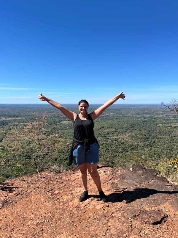 Mulher de braços abertos no alto do Morro do Chapéu, com a planície e o céu azul atrás