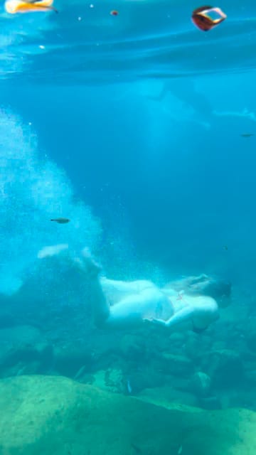 Mulher nadando sob a água azul, sobre as pedras do fundo